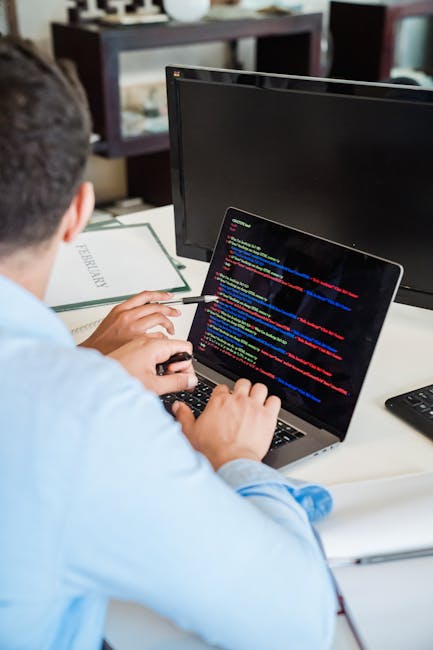 A close-up view of a laptop computer on a desk, displaying lines of HTML code in a text editor on the left side of the screen and a simple digital calculator interface with orange buttons and black sy