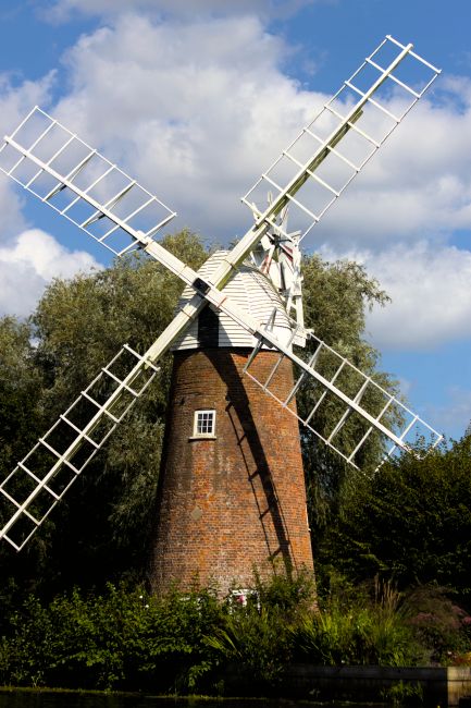An aerial view of a residential area featuring a traditional windmill situated amongst rows of brick houses and terraced homes. The windmill has white blades and a dark, conical roof, positioned centr